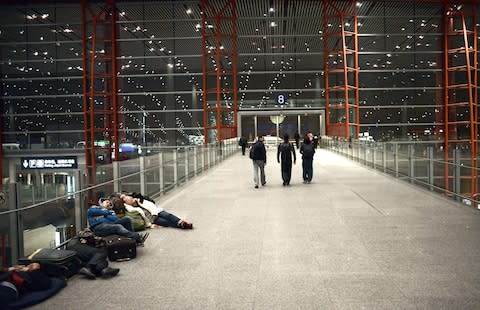 Travellers sleeping at Beijing Capital International airport in 2015 after snow storms resulted in long delays - Credit: Getty
