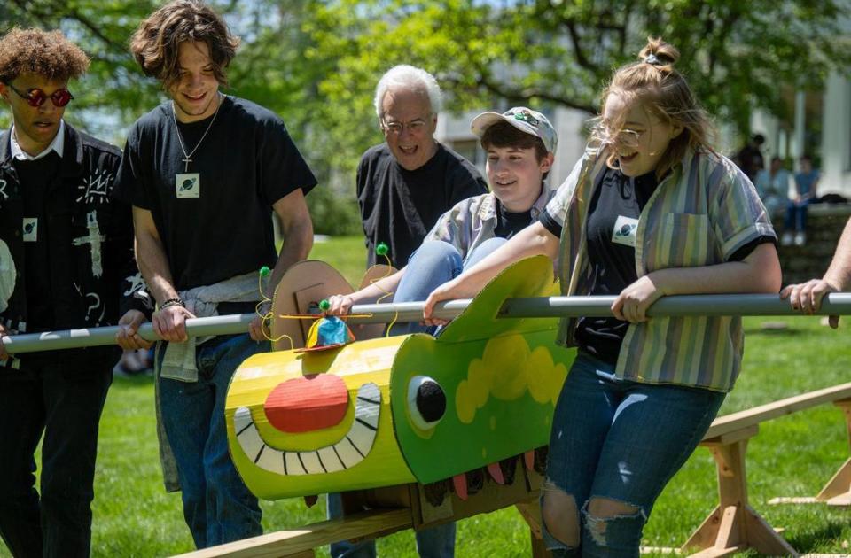 Illustration professor Steve Mayse, third from left, cheers on sophomore Sara Baum of Festus, Missouri, in her Rail Day contraption on the lawn of the Jannes Library & Learning Center at the Kansas City Art Institute.