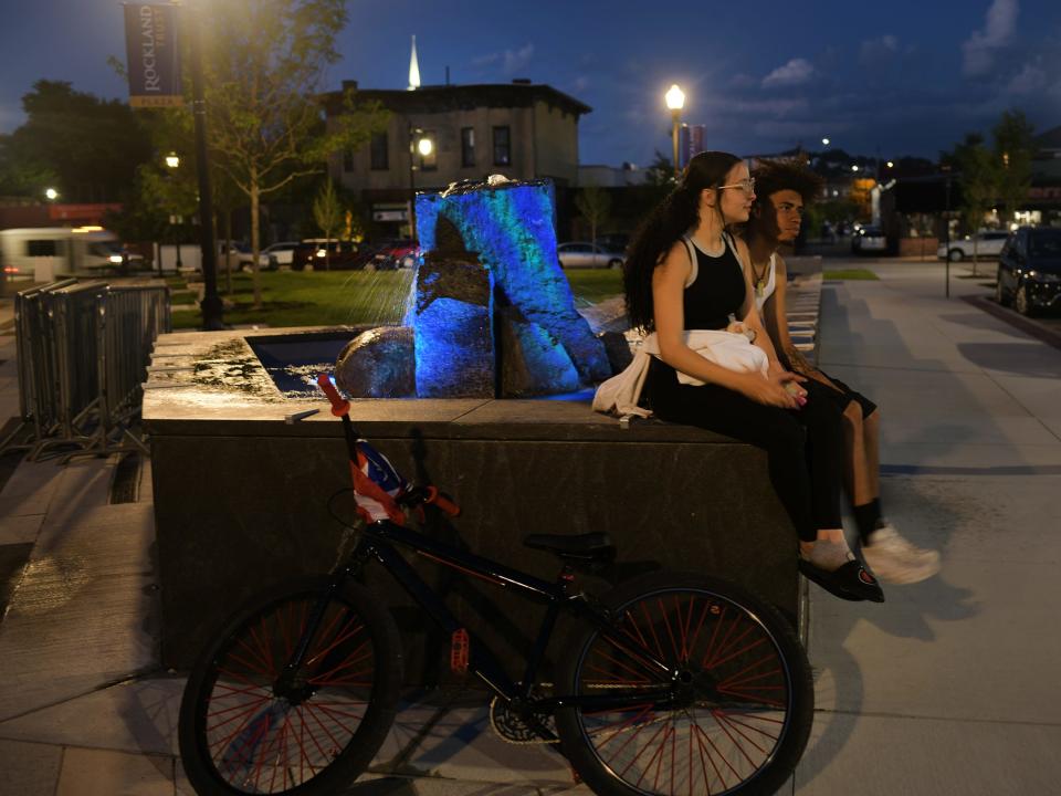 A couple sits atop the new fountain at General Josiah Pickett Memorial Grove at Rockland Trust Plaza Friday at night in the city.