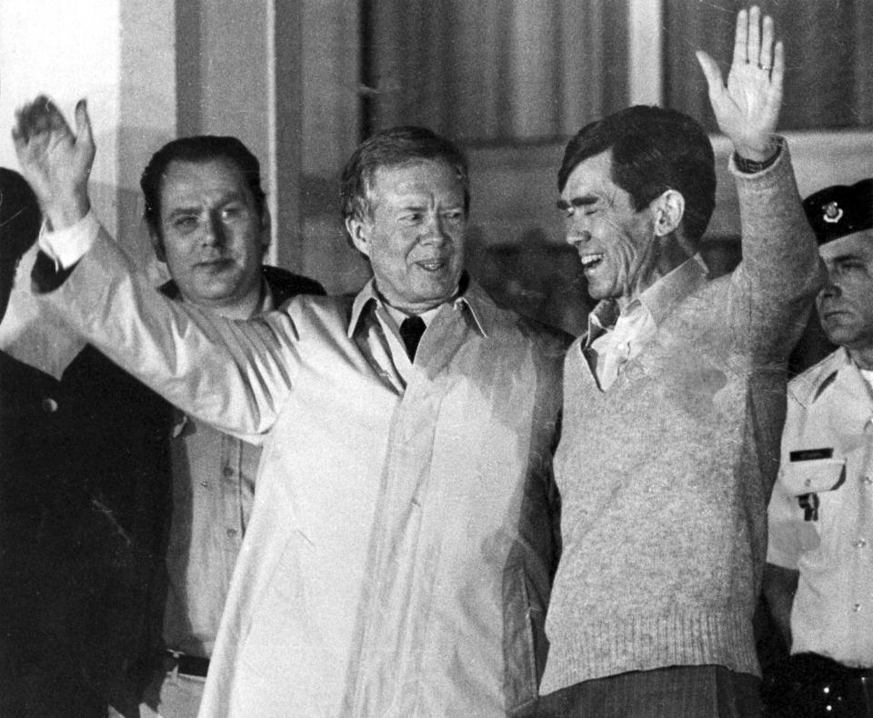 FILE - Former U.S. President Jimmy Carter, who had negotiated for the hostages release right up to the last hours of his presidency, waves to the crowd while putting his other hand around the shoulders of a former hostage in Iran, believed to be Bruce Laingen, at U.S. Air Force Hospital in Wiesbaden, Germany, Jan. 21, 1981. As Carter receives home hospice care at the age of 98, misconceptions about his life are coming into focus. Most are rooted in some truth but need more context. (AP Photo/Mark Goecks, File)