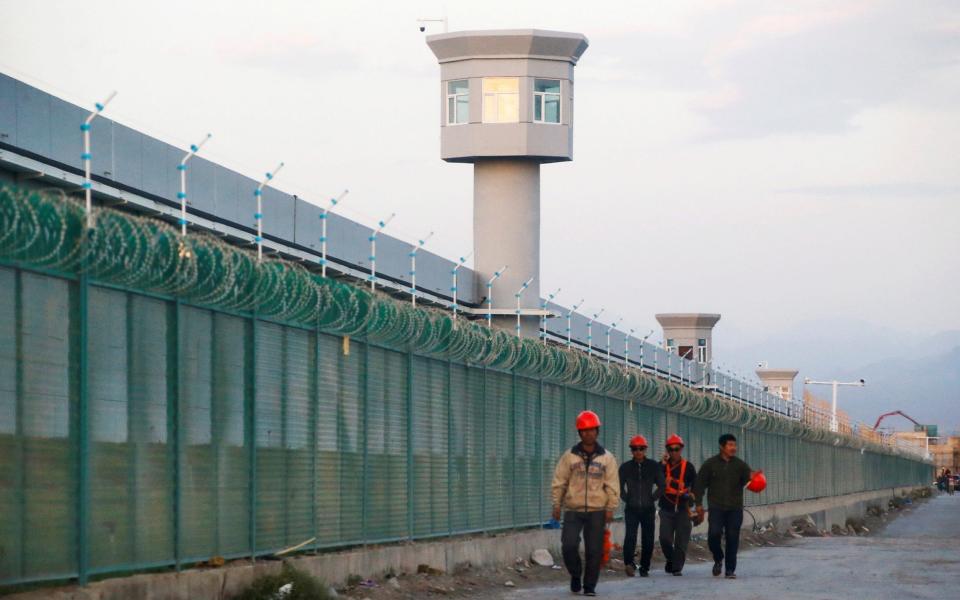 Workers walk by the fence of a Uighur internment camp in Dabancheng - Reuters
