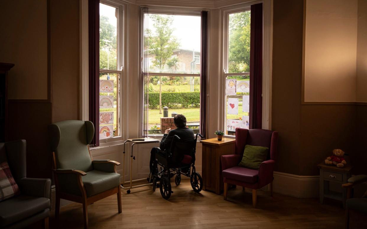 A man in a care home sitting in a wheelchair, looking out of the window, with his back to the camera
