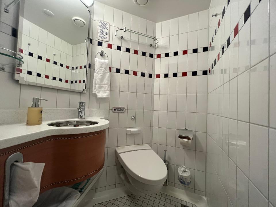 A tiled bathroom with a white toilet, sink, and mirror. 