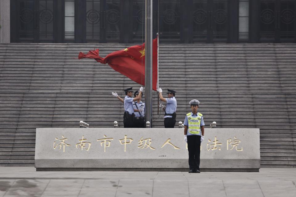 Policemen hoist a Chinese national flag in front of an entrance of the Jinan Intermediate People's Court where the trial of disgraced Chinese politician Bo will be held, in Jinan