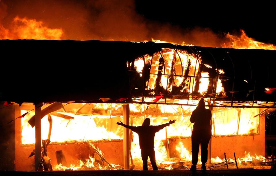 FILE - In this Nov. 25, 2014 file photo, protesters take their pictures in front of a burning building set afire by protesters in Ferguson, Mo., after the police shooting of Michael Brown. St. Louis wants to spend nearly $10 million to hire and train 160 police officers in response to a recent violent crime hike its mayor and police chief blame on a “Ferguson effect.” (AP Photo/St. Louis Post-Dispatch, Robert Cohen, File)