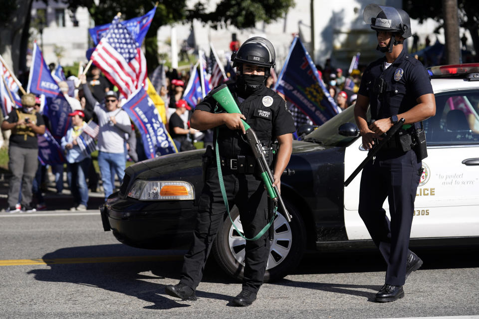 Police officers hold weapons in front of a crowd of President Donald Trump supporters outside of City Hall Wednesday, Jan. 6, 2021, in Los Angeles. Demonstrators supporting President Trump are gathering in various parts of Southern California as Congress debates to affirm President-elect Joe Biden's electoral college victory. (AP Photo/Marcio Jose Sanchez)