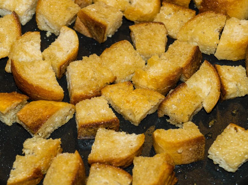 Croutons cooking in oil on a black baking sheet