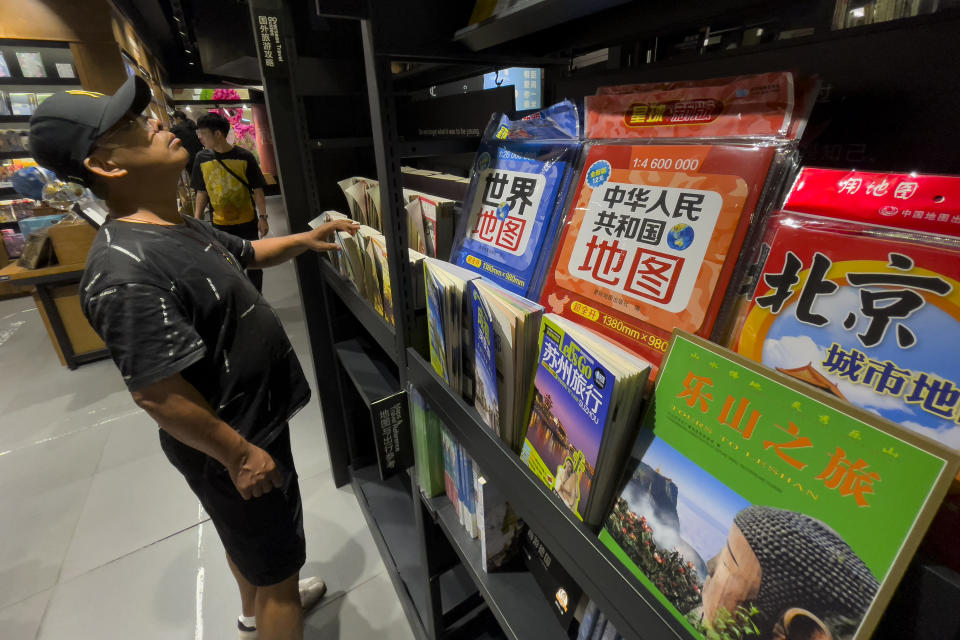 People browse for books near the new China and world map which printed on January this year on display for sale at a bookstore in Beijing, Friday, Sept. 1, 2023. China has upset many in the Asia-Pacific region with the release of a new official map that lays claim to most of the South China Sea, as well as contested parts of India and Russia, and official objections continue to mount. (AP Photo/Andy Wong)