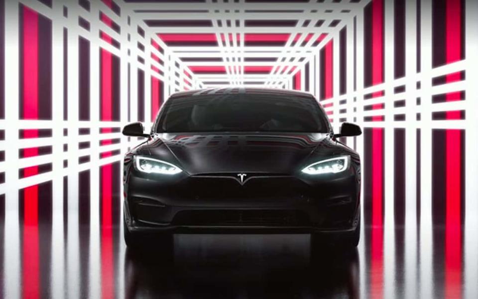 A sleep black Tesla car sits face on to the camera, framed by a corridor of bright white and red neon in a plaid pattern - Telegraph/Tesla