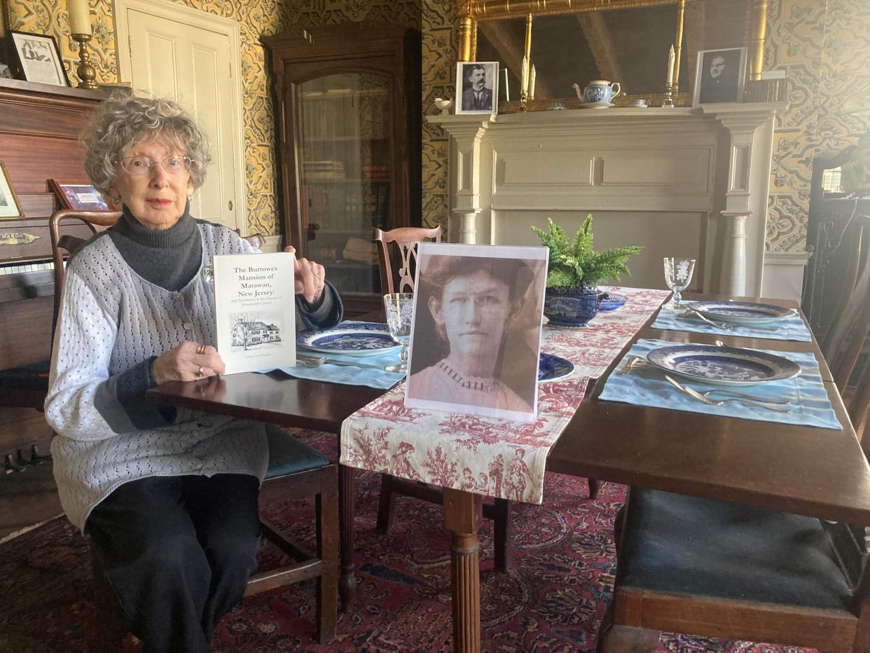 Mary Lou Diecker holds her updated book in the dining room of Burrowes Mansion in Matawan.