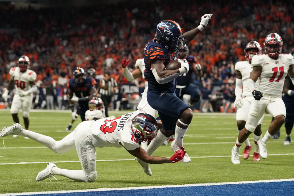 UTSA running back Sincere McCormick (3) leaps through the hands of Western Kentucky defensive back Miguel Edwards (13) for a touchdown during the second half of an NCAA college football game for the Conference USA championship Friday, Dec. 3, 2021, in San Antonio. (AP Photo/Eric Gay)