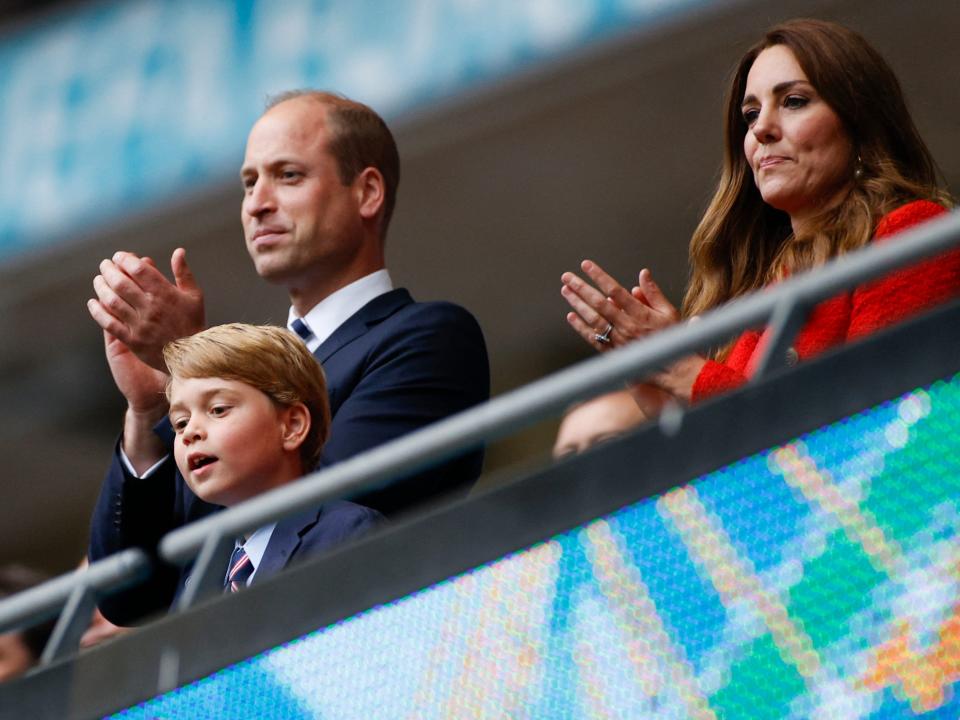 Prince George leans over a railing at a football match