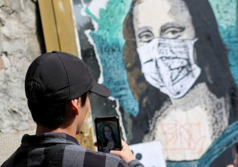 Tourist takes a picture of an image of Mona Lisa with a protective face mask after further cases of coronavirus were confirmed in Barcelona