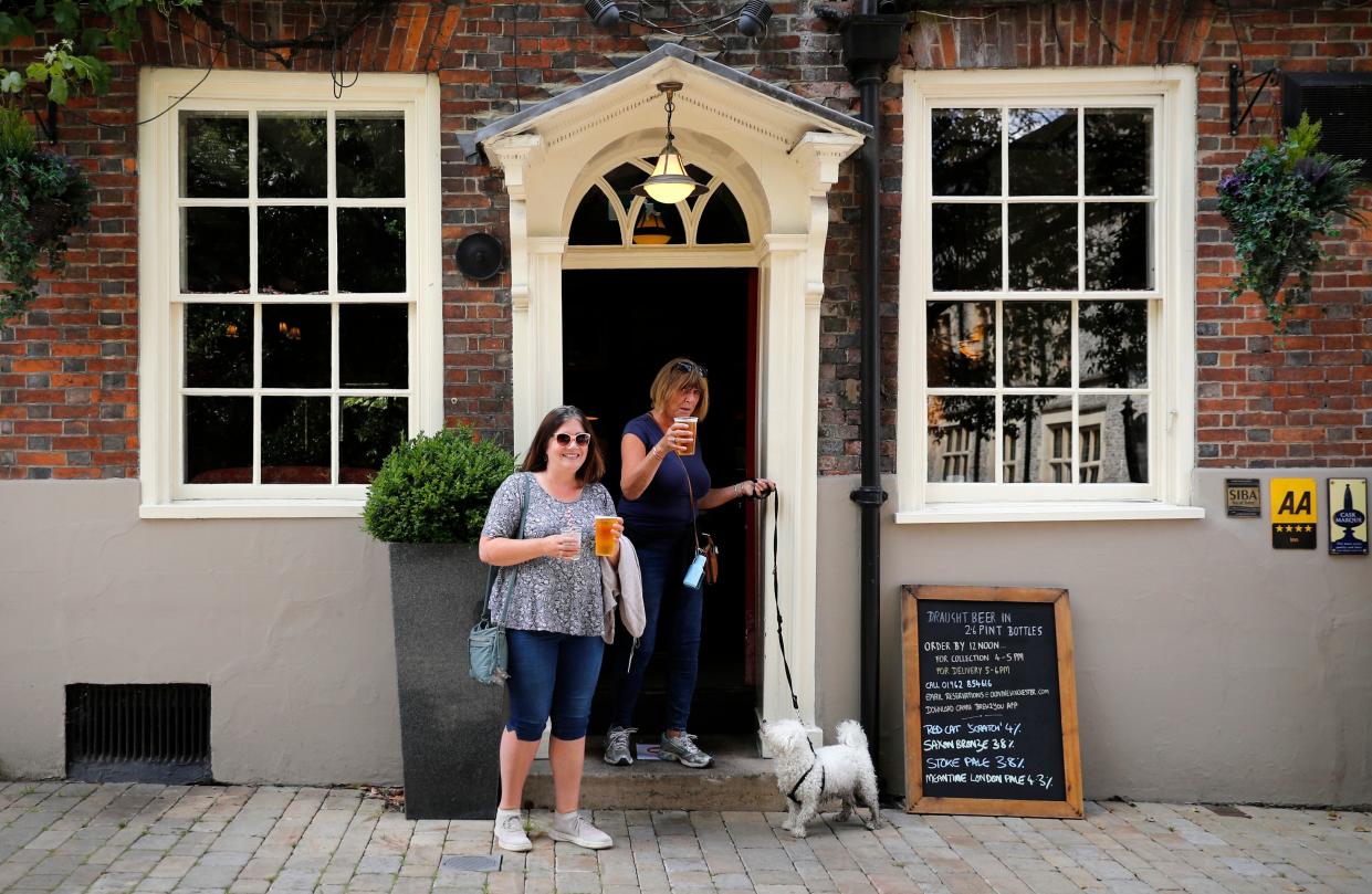 Two women walk out of The Old Vine pub with their takeaway beer in Winchester, southern England on June 7, 2020. - The UK government said Sunday it will reopen places of worship for individual prayer on June 15 as it reportedly looks to speed up easing measures in order to save jobs. Prime Minister Boris Johnson's office said services and worship groups will still be banned for the time being due to concern that the new coronavirus spreads more quickly in enclosed spaces. (Photo by ADRIAN DENNIS / AFP) (Photo by ADRIAN DENNIS/AFP via Getty Images)