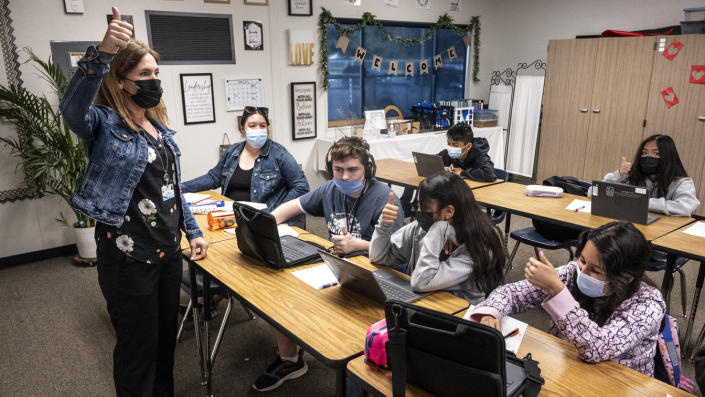 A teacher, wearing a face mask, gives students, all wearing face masks, a thumbs-up.