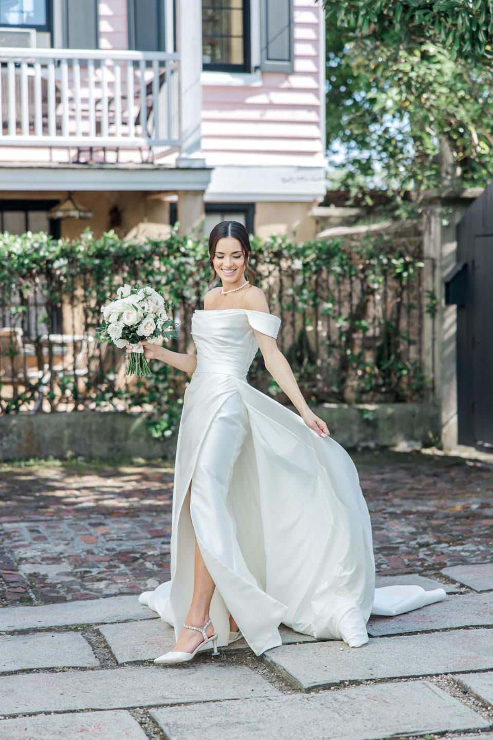 A bride twirls in her wedding dress in front of a pink house.