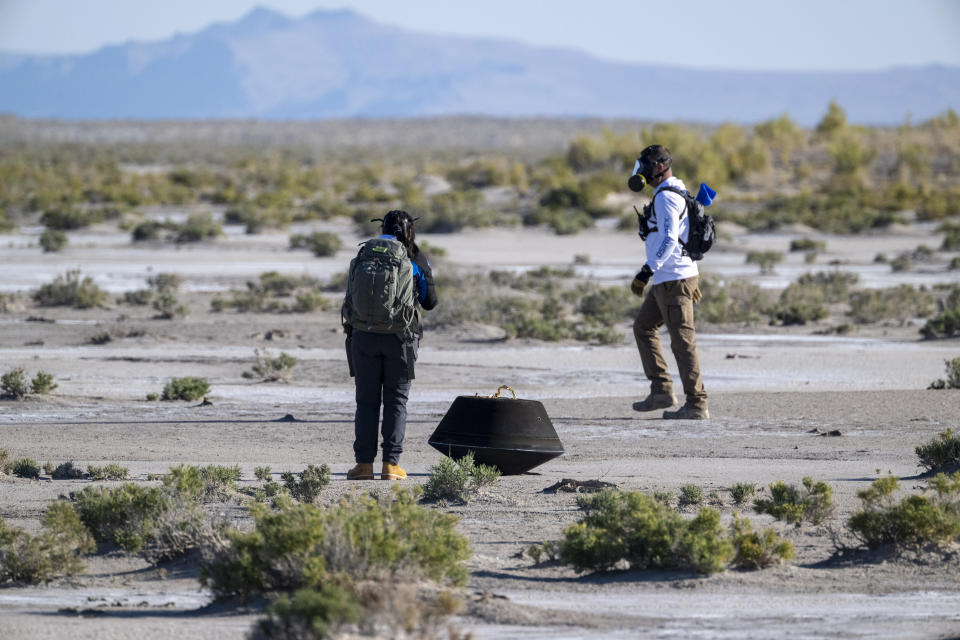 In this photo provided by NASA, Lockheed Martin System Safety Engineer Victoria Thiem, left, and On Scene Commander of Recovery Stuart Wylie, right, perform preliminary checks on the sample return capsule from NASA's Osiris-Rex mission after touching down in the desert, at the Department of Defense's Utah Test and Training Range on Sunday, Sept. 24, 2023. The sample was collected from the asteroid Bennu in October 2020. (Keegan Barber/NASA via AP)