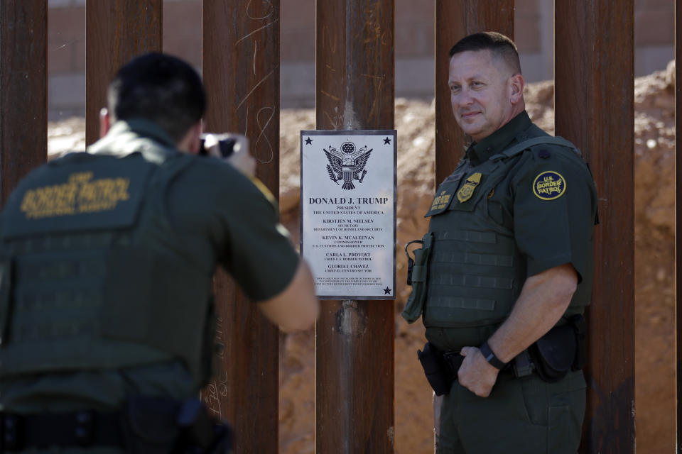 FILE - In this Oct. 26, 2018, file photo, Border Patrol agent Michael Sullivan, right, poses for a picture next to a plaque adorning a newly fortified border wall structure in Calexico, Calif. President Donald Trump is visiting Calexico on Friday, April 5, 2019, to tour a recently-built portion of the border fence that bears the silver plaque with his name on it. (AP Photo/Gregory Bull, File)