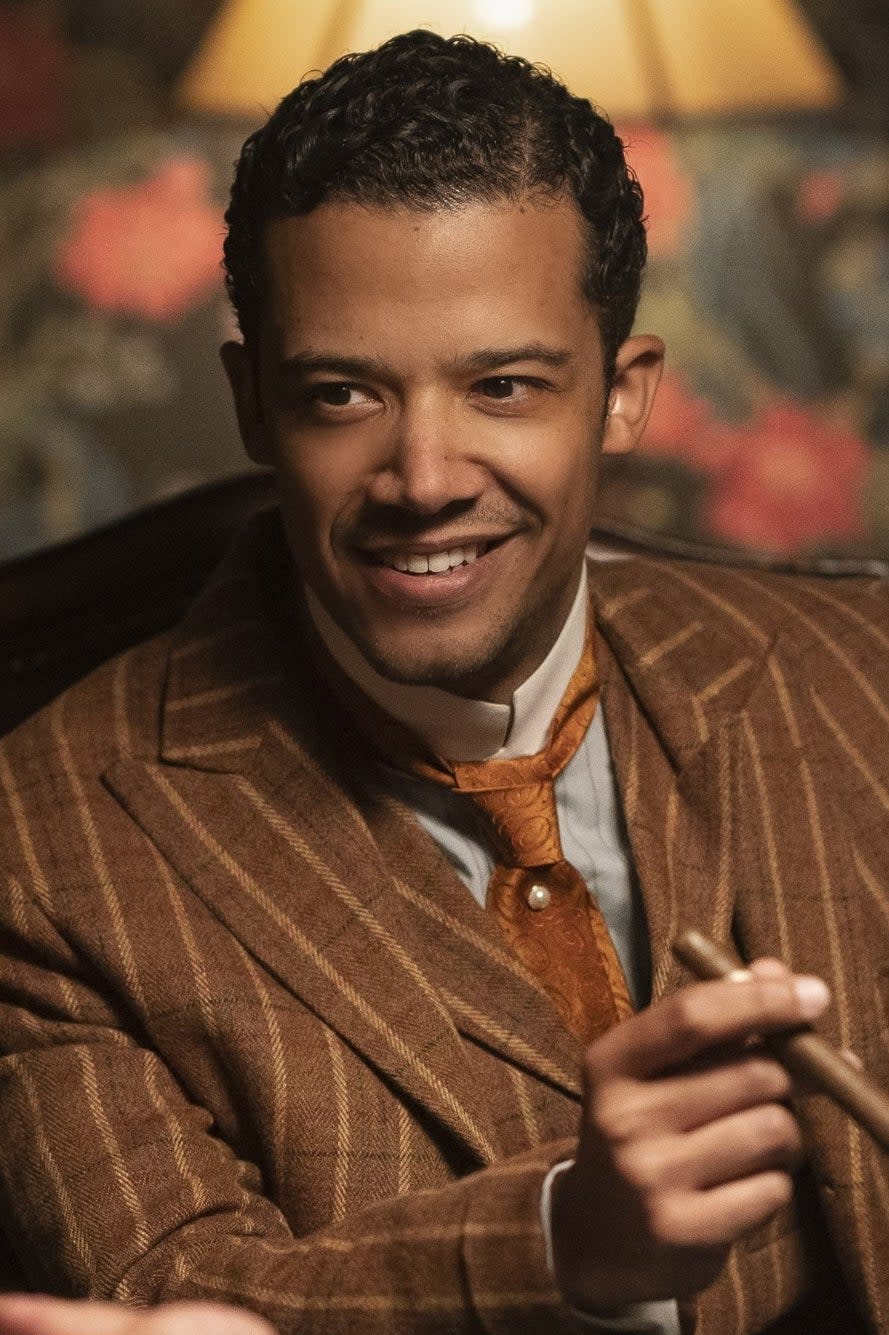 Jacob as Louis in a poker game holding cards, wearing a patterned jacket, smiling confidently at the table