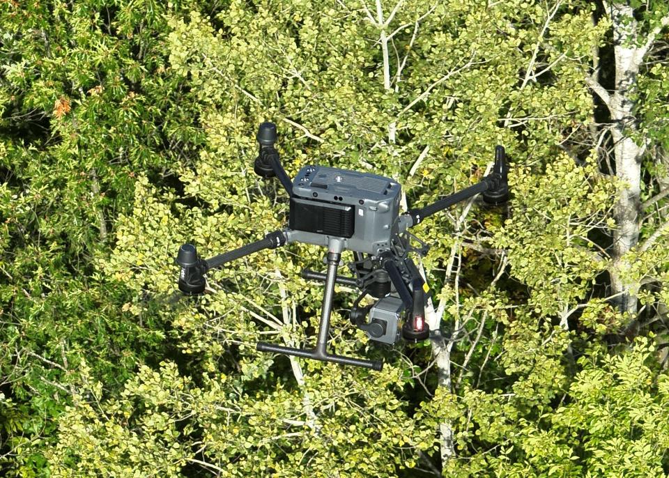 A drone is photographed as it flies over a wooded area.