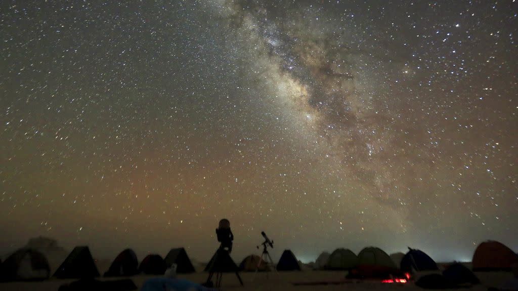 The 'Milky Way' is seen in the night sky around telescopes and camps of people over rocks in the White Desert north of the Farafra Oasis southwest of Cairo