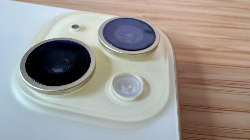 A yellow iPhone 15 on a wooden desk