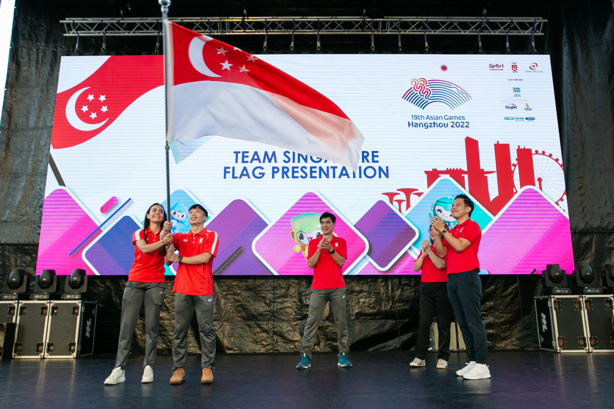 Team Singapore flag bearers Amita Berthier (left) and Jowen Lim hold aloft the national flag during the flag presentation ceremony for the 2023 Asian Games. (PHOTO: SNOC/Wee Teck Hian)