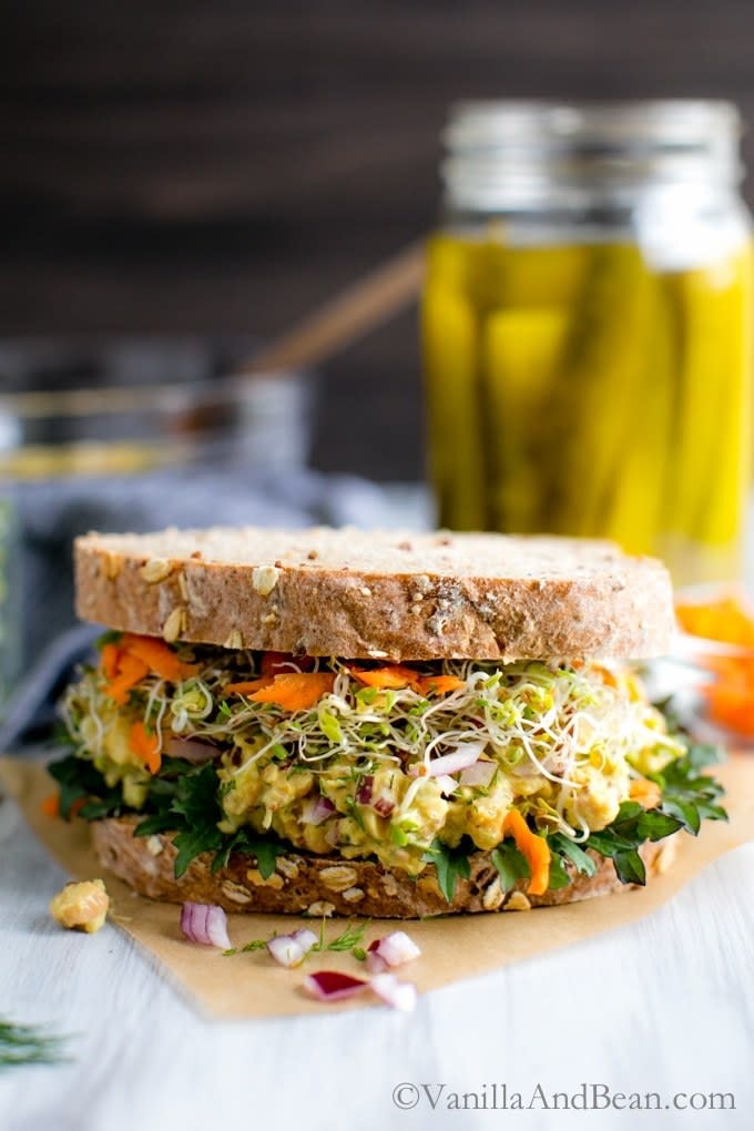 A large grainy sandwiched is filled with sprouts and smashed chickpea salad.