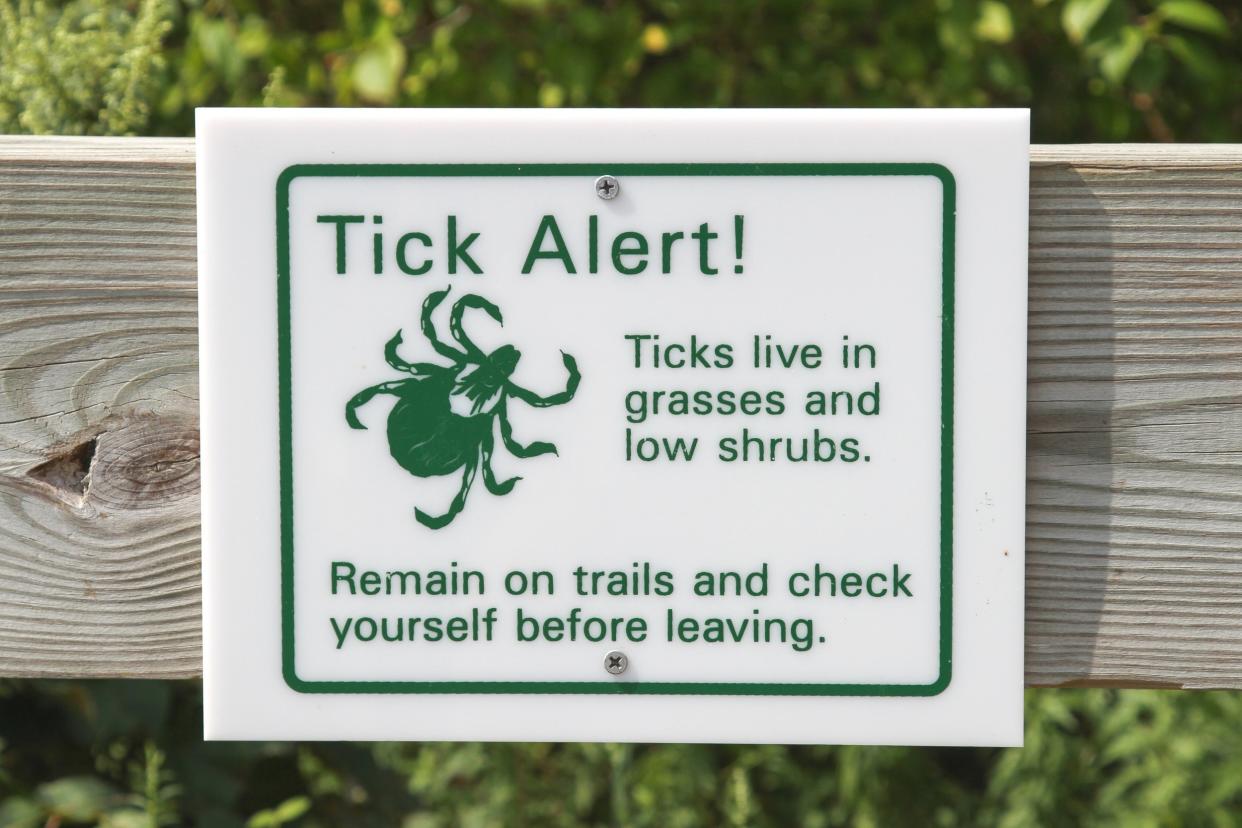 Green and White Tick Warning Sign on a Post