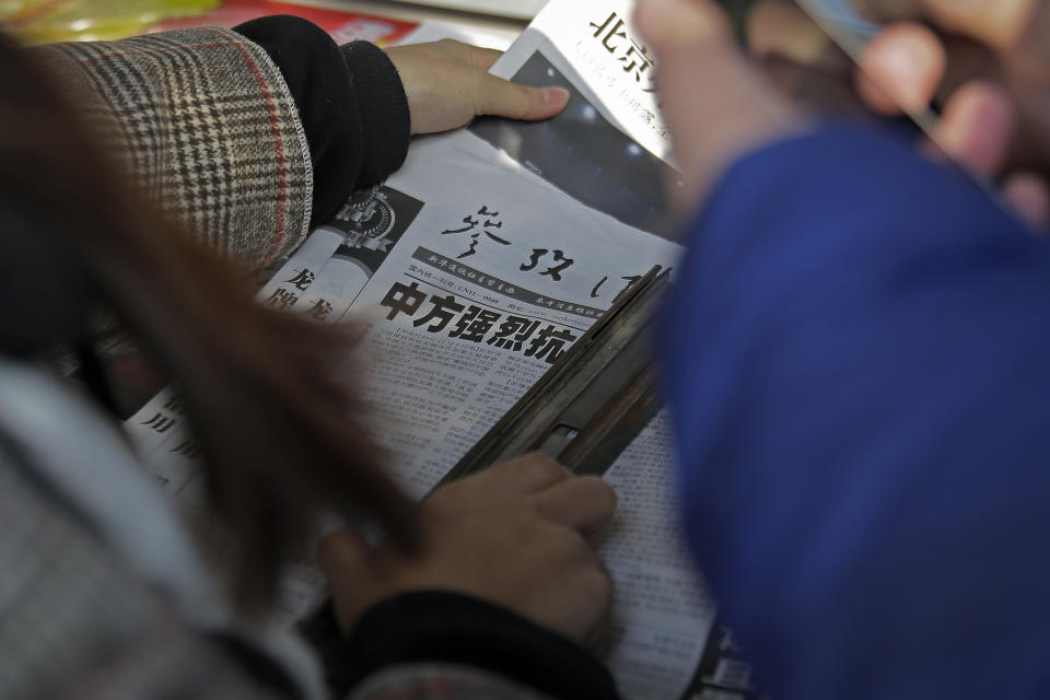 A woman takes a copy of a newspaper near another with the headline of China outcry against U.S. on the detention of Huawei's chief financial officer, Meng Wanzhou, at a news stand in Beijing, Monday, Dec. 10, 2018. China has summoned the U.S. ambassador to Beijing to protest Canada's detention of an executive of Chinese electronics giant Huawei at Washington's behest and demand the U.S. cancel an order for her arrest. (AP Photo/Andy Wong)