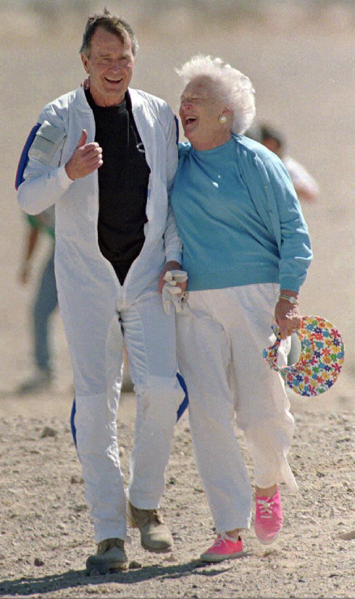 FILE - In this March 25, 1997, file photo, former President George H.W. Bush gets a hug from his wife Barbara after he made a successful parachute jump at the U.S. Army's Yuma Proving Ground outside of Yuma, Ariz. Both Bushes have been hospitalized this week in Houston, where the former president is being treated for pneumonia and his wife for bronchitis. George Bush is 92 and Barbara is 91. (AP Photo/Mike Nelson, Pool, File)