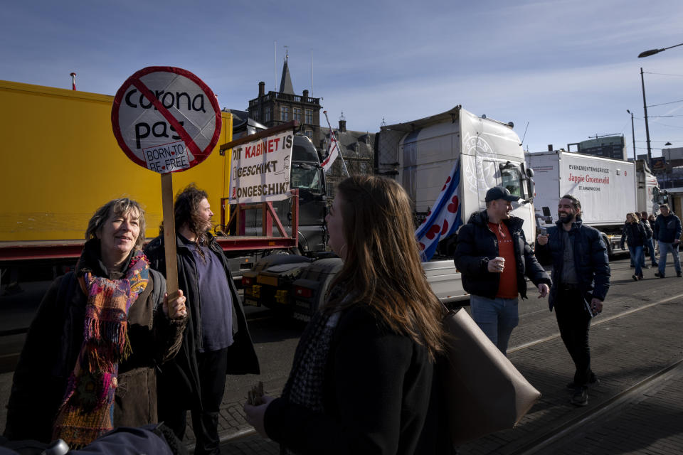 Demonstrators talk as some 20 trucks blocked one entrance to the government buildings, rear, in The Hague, Netherlands, Saturday, Feb. 12, 2022, to protest against COVID-19 restrictions. The events are in part inspired by protesters in Canada. (AP Photo/Peter Dejong)