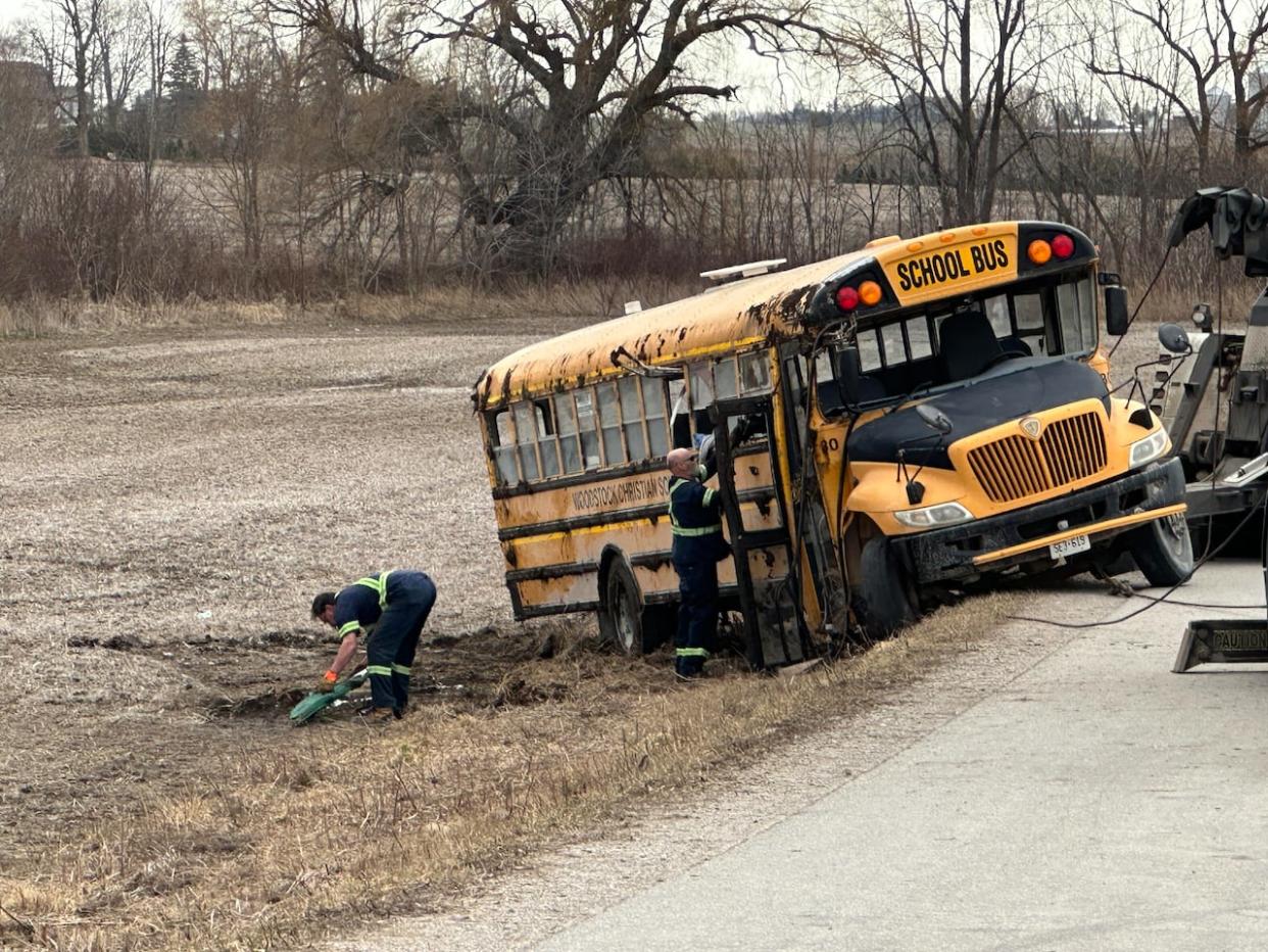 Tow truck drivers are trying to lift up the bus that rolled over on its side, south of Woodstock, Ont.  A child was airlifted to hospital and four other students had minor injuries. The 34-year-old bus driver has been charged with careless driving causing bodily harm.  (Kate Dubinski/CBC - image credit)