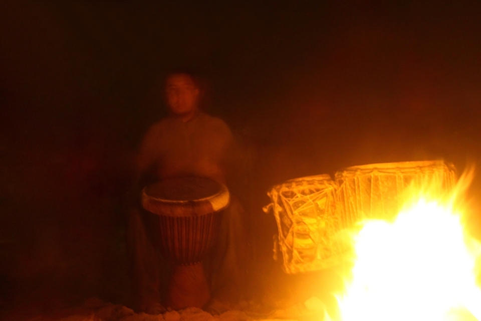 Drummer playing percussion in camp fire at night.