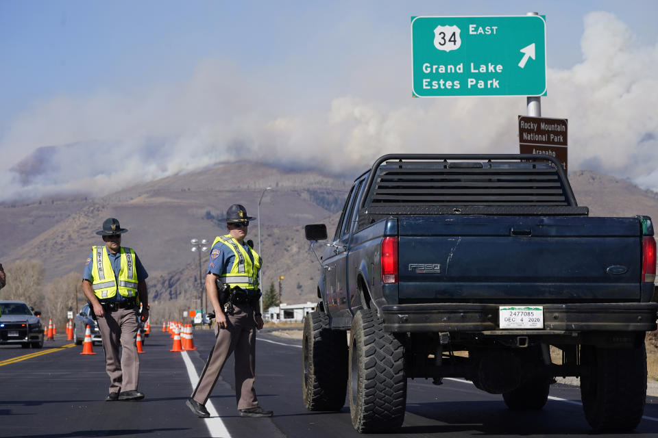 As smoke rises from mountain ridges in the background, Colorado State Patrol troopers stop a motorist on Highway 34 as a wildfire burns Thursday, Oct. 22, 2020, near Granby, Colo. (AP Photo/David Zalubowski)