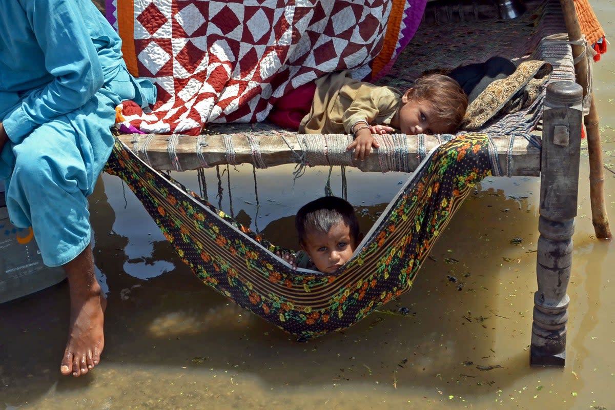 Flood-affected children sit on a traditional cot alongside flood waters after heavy monsoon rains in the Jaffarabad district of Balochistan province on 31 August  (AFP via Getty)