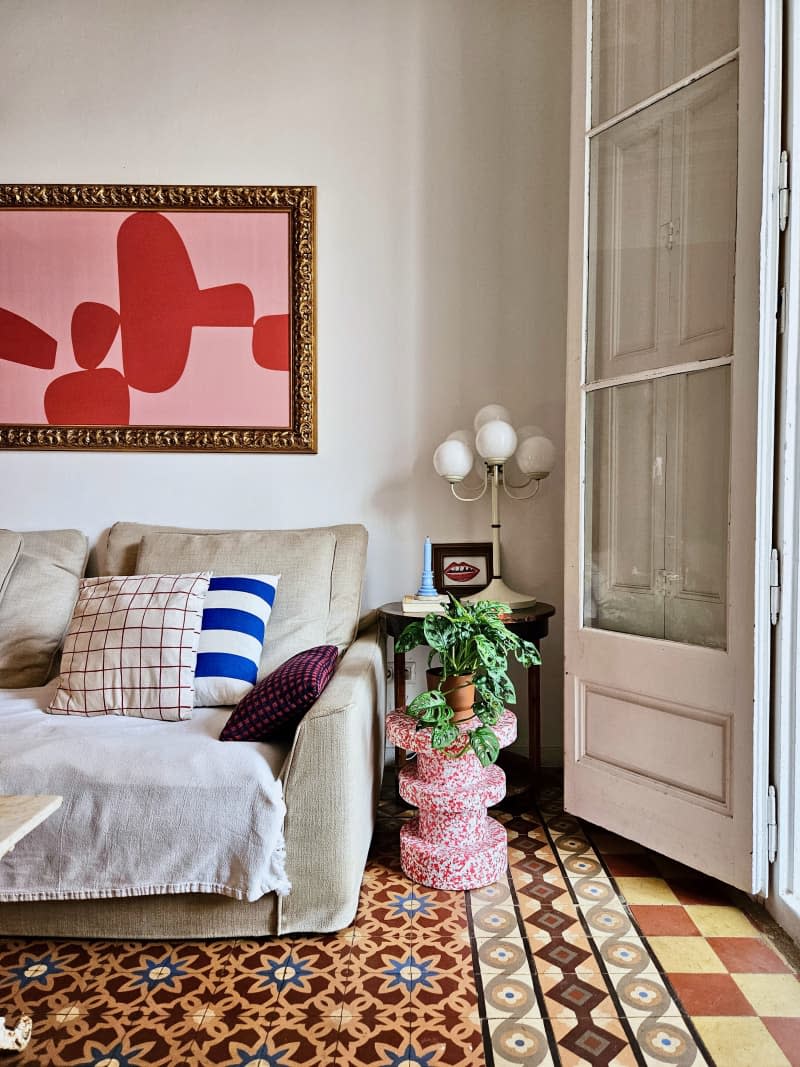 Framed artwork above a couch with a decorative side table with planted plants.