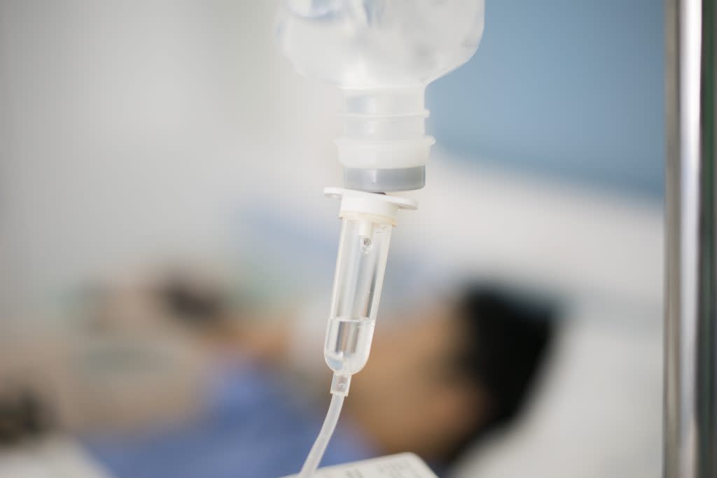 A closeup of an IV drip with a patient in the background.