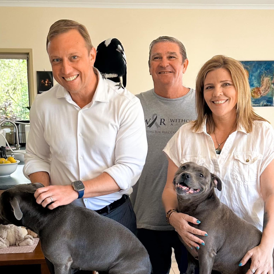 Premier Steven Miles beams as he allows Molly the magpie to perch on his shoulder. Juliette Wells and Reece Mortensen stand beside him with their dogs.