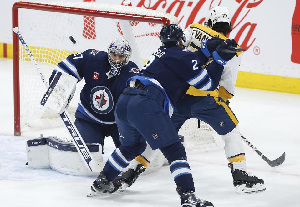 Winnipeg Jets goaltender Connor Hellebuyck (37) saves the shot from Nashville Predators' Luke Evangelista (77) as Dylan DeMelo (2) defends during the first period of an NHL hockey game, Saturday, April 8, 2023 in Winnipeg, Manitoba. (John Woods/The Canadian Press via AP)