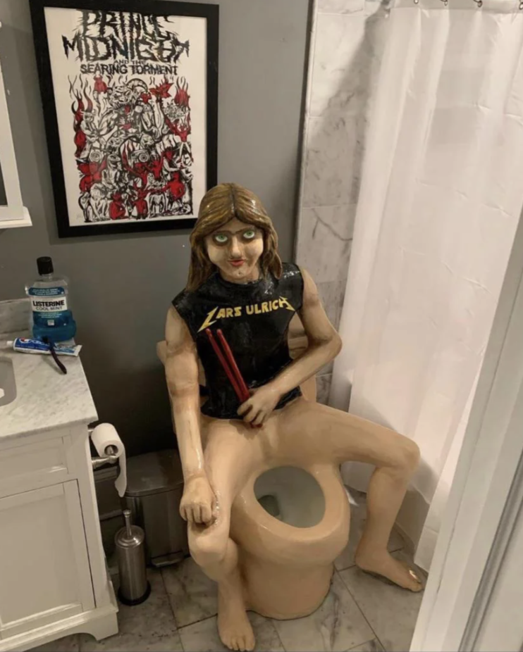 Sculpture of a person with a Lars Ulrich shirt sitting on a toilet, positioned in a bathroom next to a shower