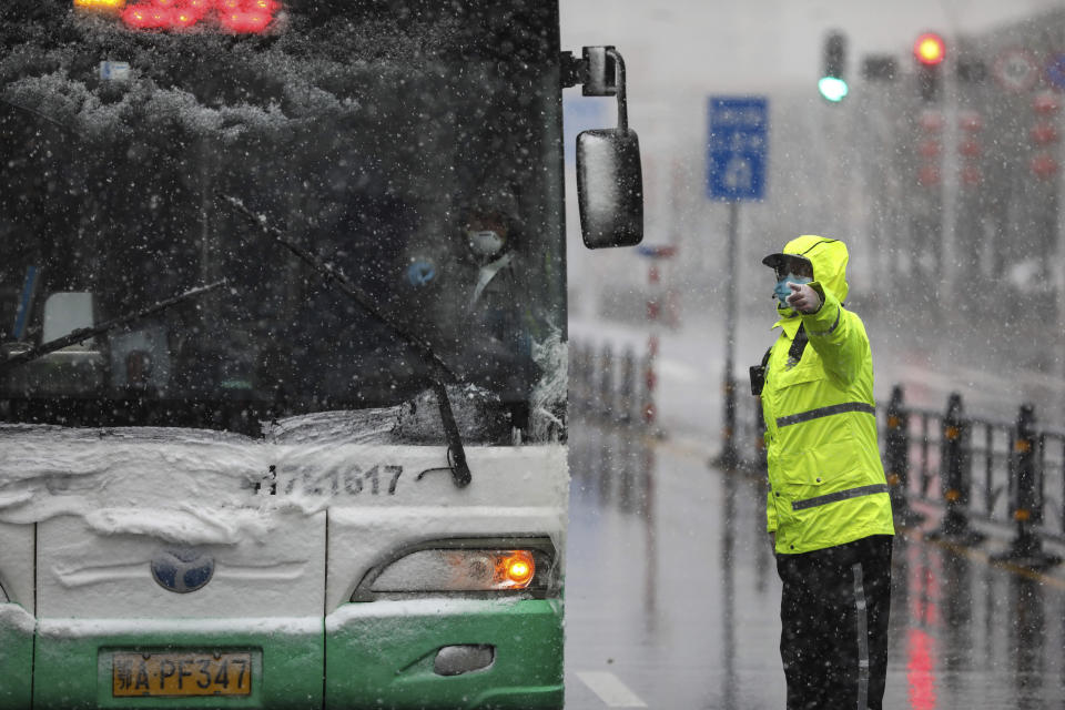 A policeman wearing a face mask directs a bus at a tumor hospital newly designated to treat COVID-19 patients in Wuhan in central China's Hubei Province, Saturday, Feb. 15, 2020. The virus is thought to have infected more than 67,000 people globally and has killed at least 1,526 people, the vast majority in China, as the Chinese government announced new anti-disease measures while businesses reopen following sweeping controls that have idled much of the economy. (Chinatopix via AP)