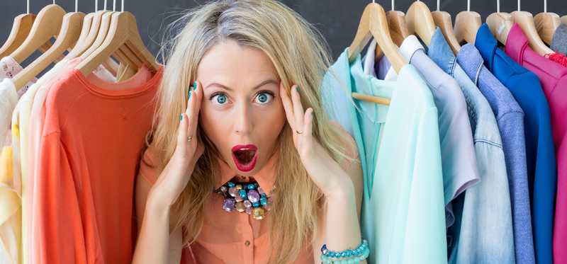 Woman standing amid a clothing rack with hands to her head.