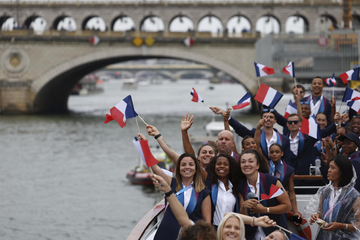 French athlete Yolaine Yengo, front center, and fellow athletes of the delegation of France wave flags as they sail in a boat on the river Seine. / Credit: Franck Fife / AP