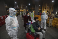 Indian municipal workers in personal protective equipment (PPE) guide passengers arriving from United Kingdom, at Chhatrapati Shivaji Maharaj International Airport in Mumbai, India, Tuesday, Dec. 22, 2020. Dozens of countries around the world slapped tough travel restrictions on the U.K. because of a new and seemingly more contagious strain of the coronavirus in England. From Canada to India, one nation after another banned flights from Britain. (AP Photo/Rafiq Maqbool)