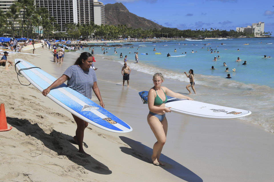 Two people with surf boards walk on Waikiki Beach, Thursday, June, 23, 2022 in Honolulu. In a major expansion of gun rights after a series of mass shootings, the Supreme Court said Thursday that Americans have a right to carry firearms in public for self-defense.