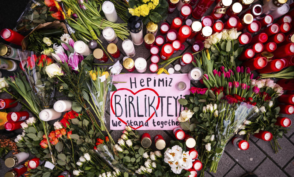 Flowers and candles and a placard with a painted heart and the inscription "We stand together", are set around a monument for the brothers Grimm, Hanau's best known sons, on the market place in Hanau, Germany, Friday, Feb. 21, 2020 two days after a 43-year-old German man shot and killed several people at several locations in a Frankfurt suburb on Wednesday, Feb. 19, 2020. (Andreas Arnold/DPA via AP)