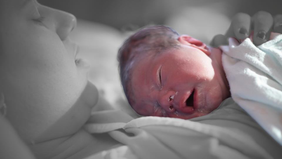 A woman holds a newborn who has a layer of vernix on his skin