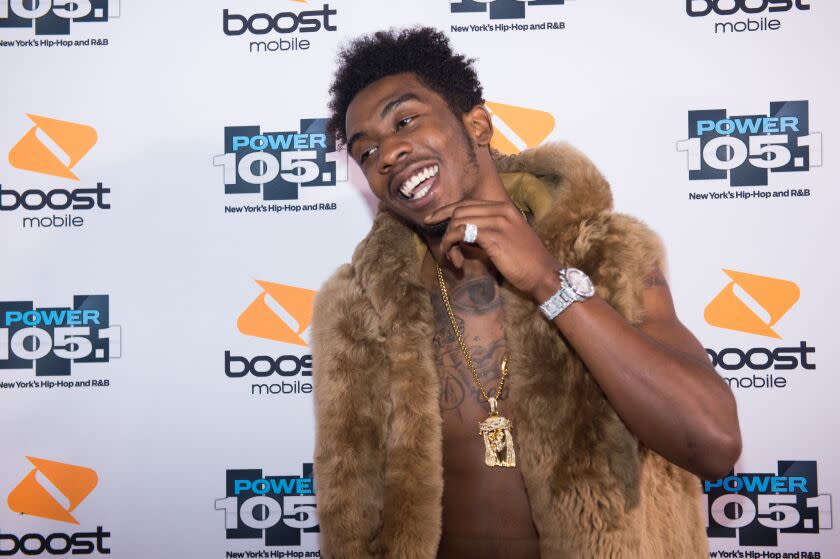 Rapper Desiigner smiling with hand under his chinm wearing a fur vest and gold chain