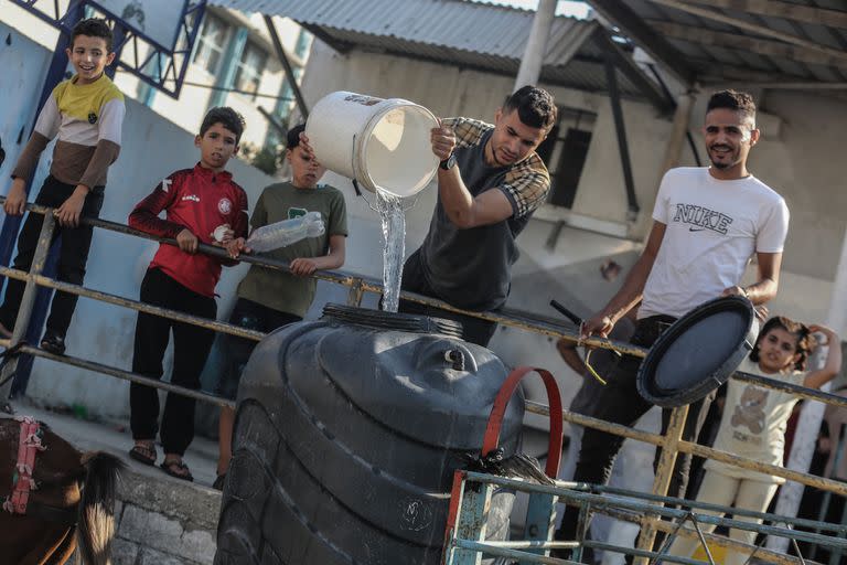 Los palestinos llenan contenedores con agua potable desde un vehículo de distribución de agua, en medio de la crisis hídrica provocada por el asedio israelí a la Franja de Gaza